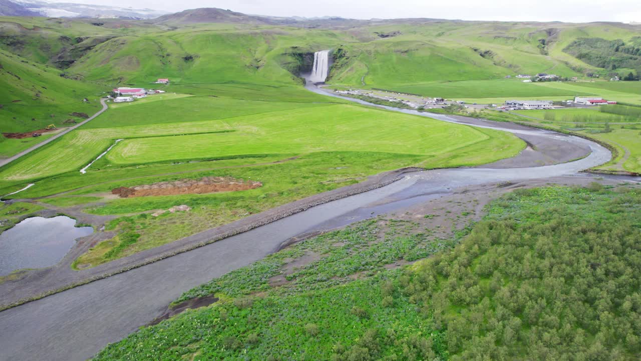 雄伟有力的斯科加弗斯瀑布从悬崖和河流在冰岛的绿色田野在夏天视频下载