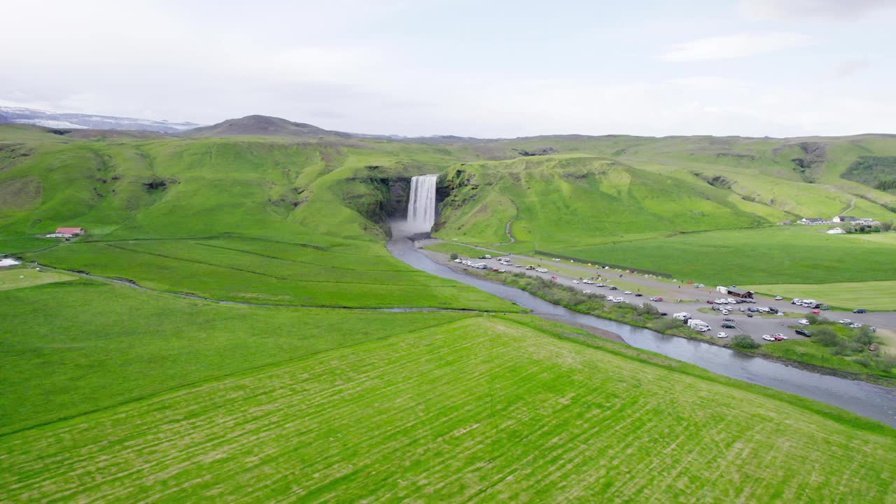 雄伟有力的斯科加弗斯瀑布从悬崖和河流在冰岛的绿色田野在夏天视频下载