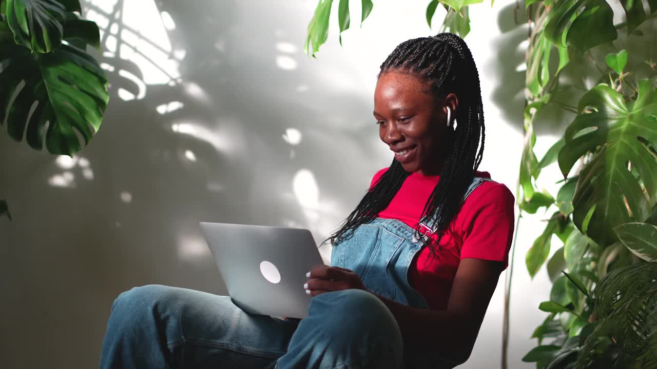 愉快的黑人女学生在家里用笔记本电脑进行视频通话，周围都是室内植物视频下载
