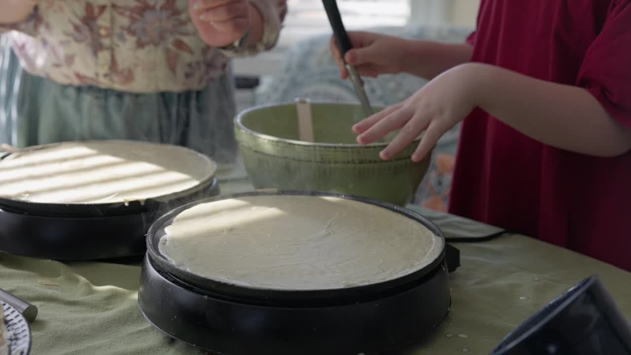 家庭主妇检查并熟练地翻转煎锅上的煎饼，指导女儿烹饪技巧。视频素材