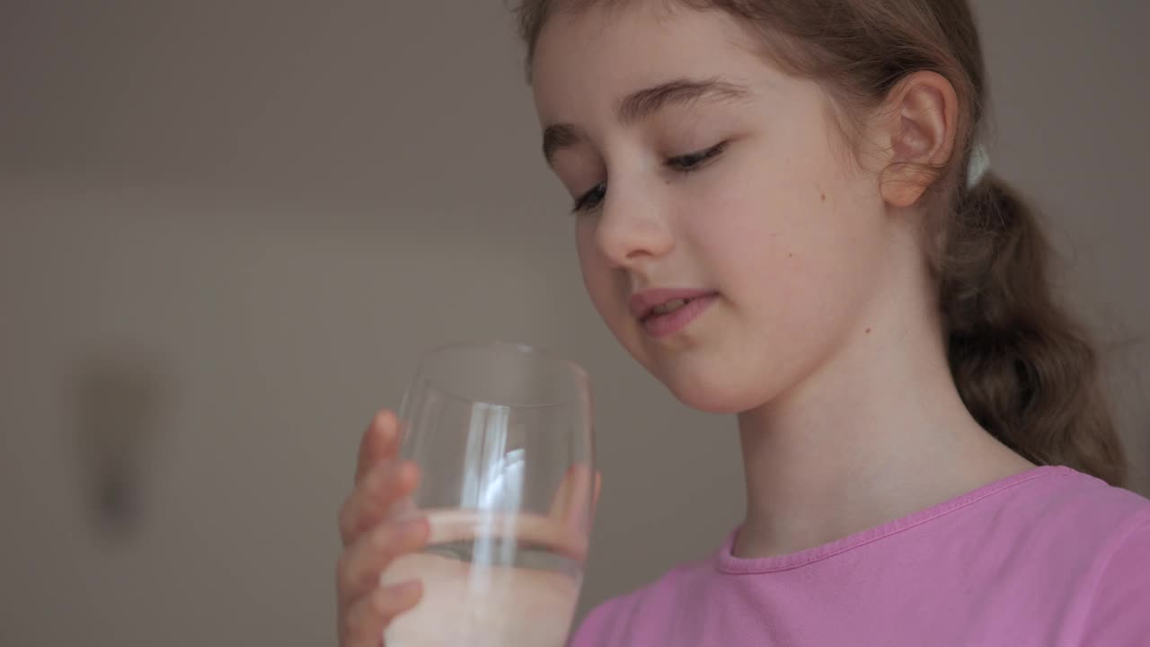 女孩从杯子里喝干净的水。儿童女孩在家里饮用玻璃新鲜透明纯过滤矿泉水。特写孩子喝杯水健康的身体护理。健康的生活方式。视频下载