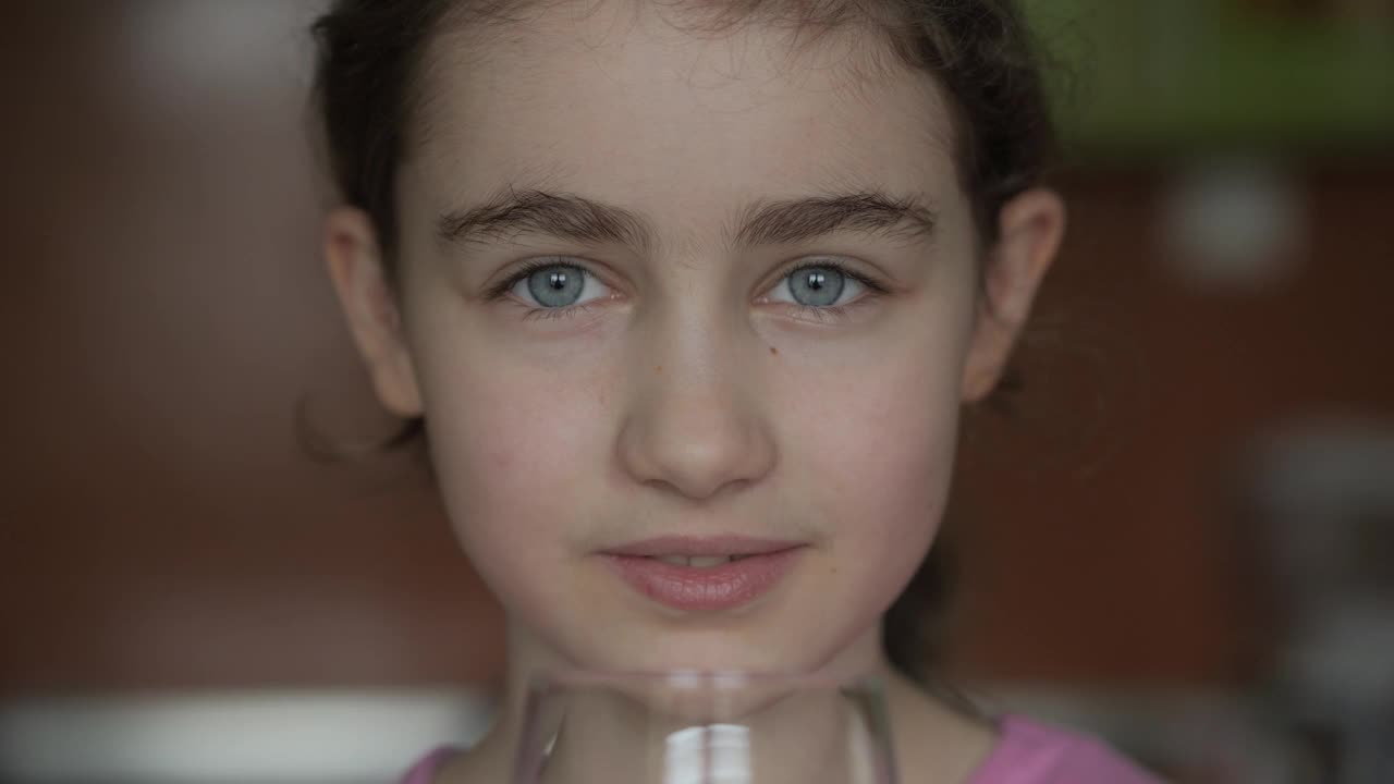 女孩从杯子里喝干净的水。儿童女孩在家里饮用玻璃新鲜透明纯过滤矿泉水。特写孩子喝杯水健康的身体护理。健康的生活方式。视频下载