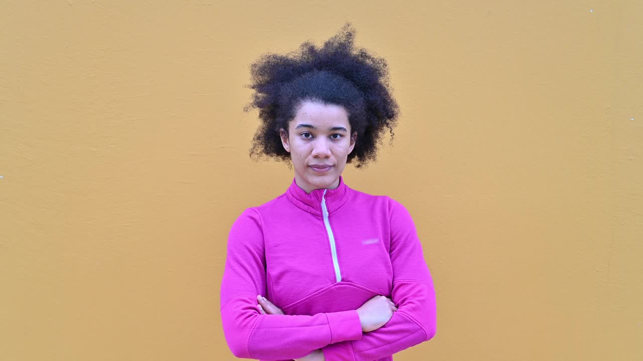坚定的千禧一代非裔美国女运动员穿着粉色运动服，在橙色墙壁旁摆姿势视频下载