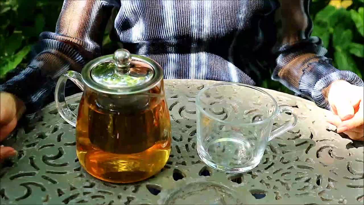 一位女士将热茶倒进花园桌上的透明杯子的镜头视频下载
