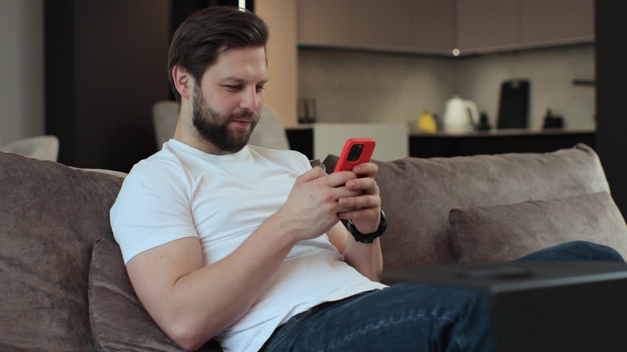 快乐的年轻人在家里舒适的客厅里使用智能手机。浏览互联网，在社交网络上查看视频。人们的生活理念。视频下载