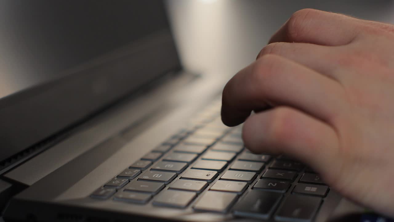 男手专业用户坐在家里用笔记本电脑键盘打字。男人的手指在电脑上敲击和发短信，上网浏览。视频下载