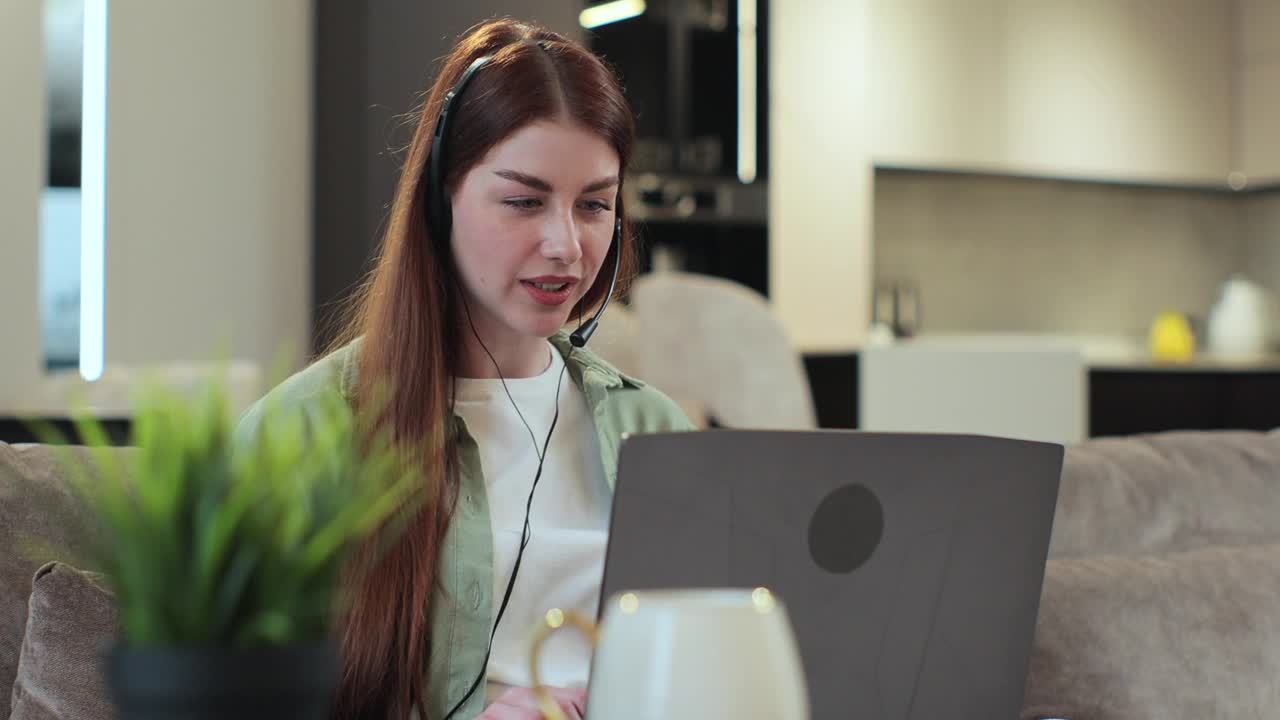 远程工作的女人戴着耳机在笔记本电脑上打字和聊天咨询，在家上网聊天。远程工作或教育的概念。视频下载
