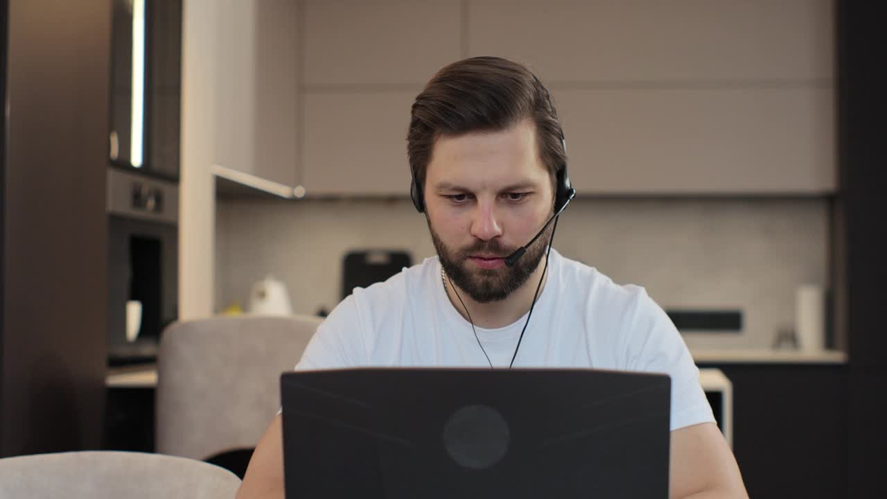 一个年轻人在家庭办公室的肖像。白人男子在家里和同事开会。男性经理在远程办公场所盯着笔记本电脑屏幕。视频下载