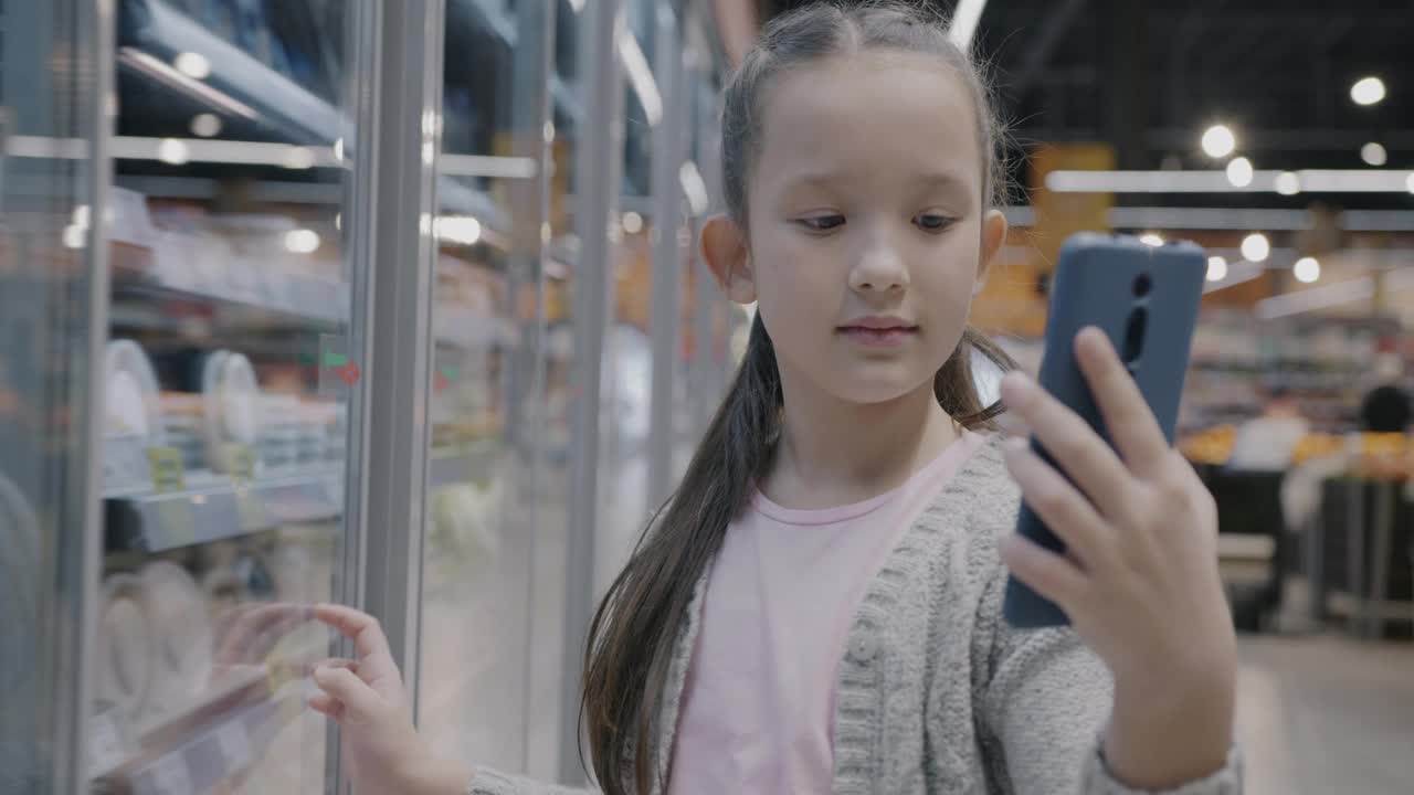可爱的小女孩用智能手机在线视频通话，指着超市里的食物视频下载