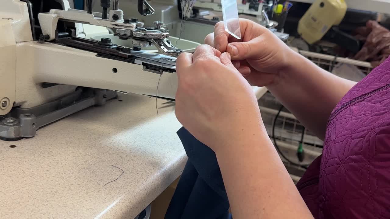 纺织工业。圈和纽扣。工业缝纫设备。紧固缝纫机。一个女孩正在给一件蓝色衬衫缝纽扣视频下载