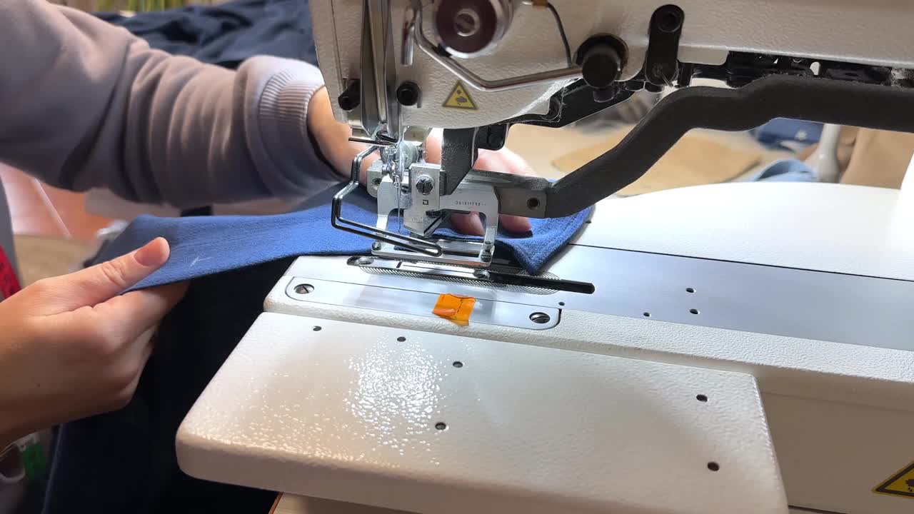 纺织工业。圈和纽扣。工业缝纫设备，一种打环的机器。这个女孩在一件蓝色衬衫上打环视频下载