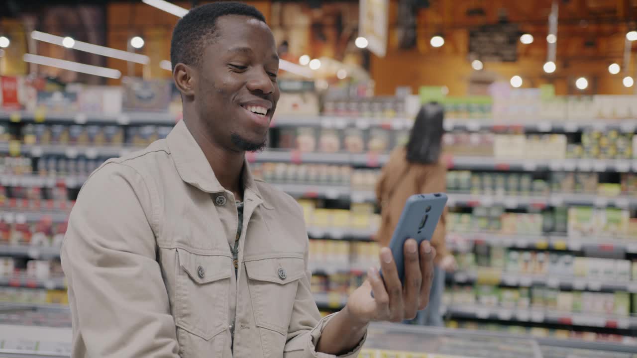 快乐的非洲裔美国人在超市展示食物，用智能手机在线视频通话视频下载