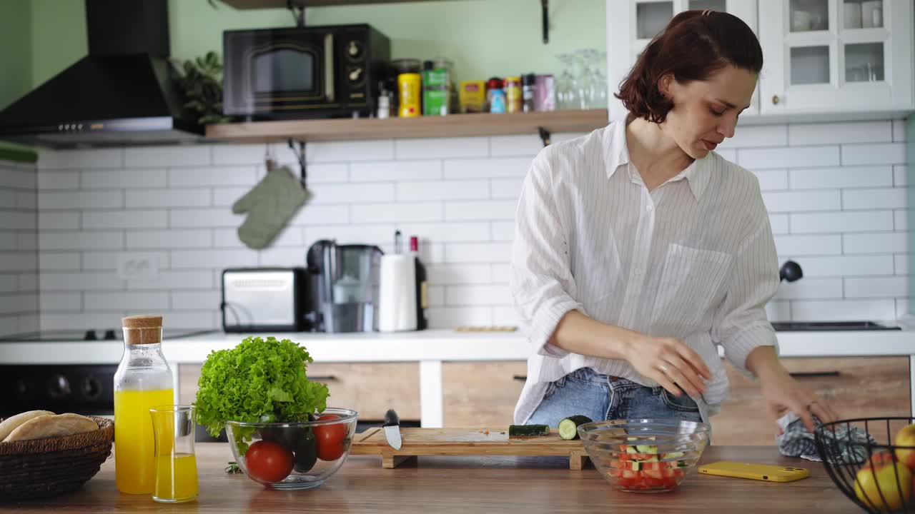 一位年轻的白人妇女在做饭时使用手机视频下载