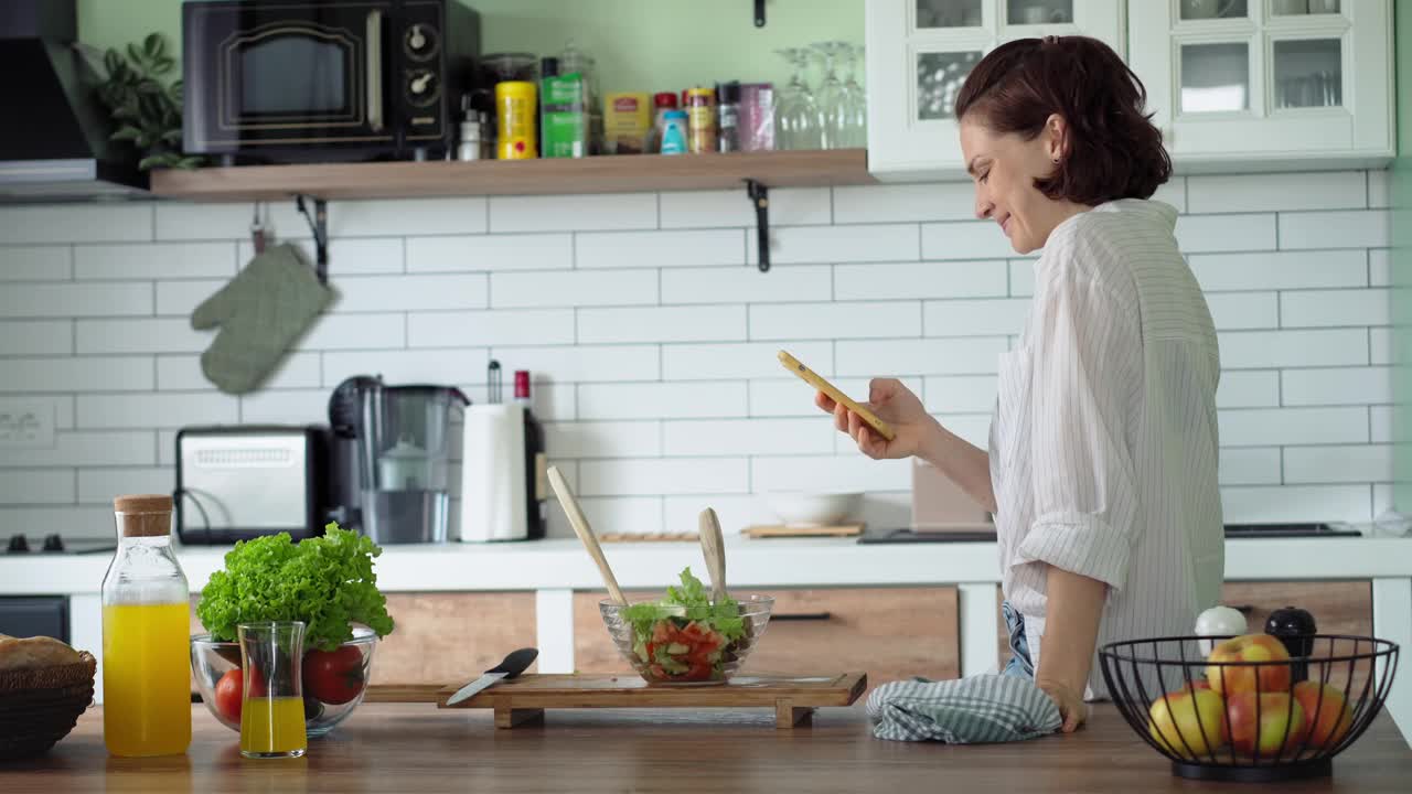 一位年轻的白人妇女在做饭时使用手机视频下载