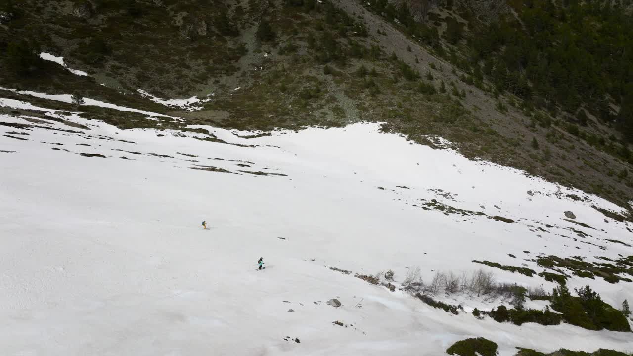 两个滑雪者在草地间的雪地上飞快地滑下峡谷。鸟瞰图视频下载