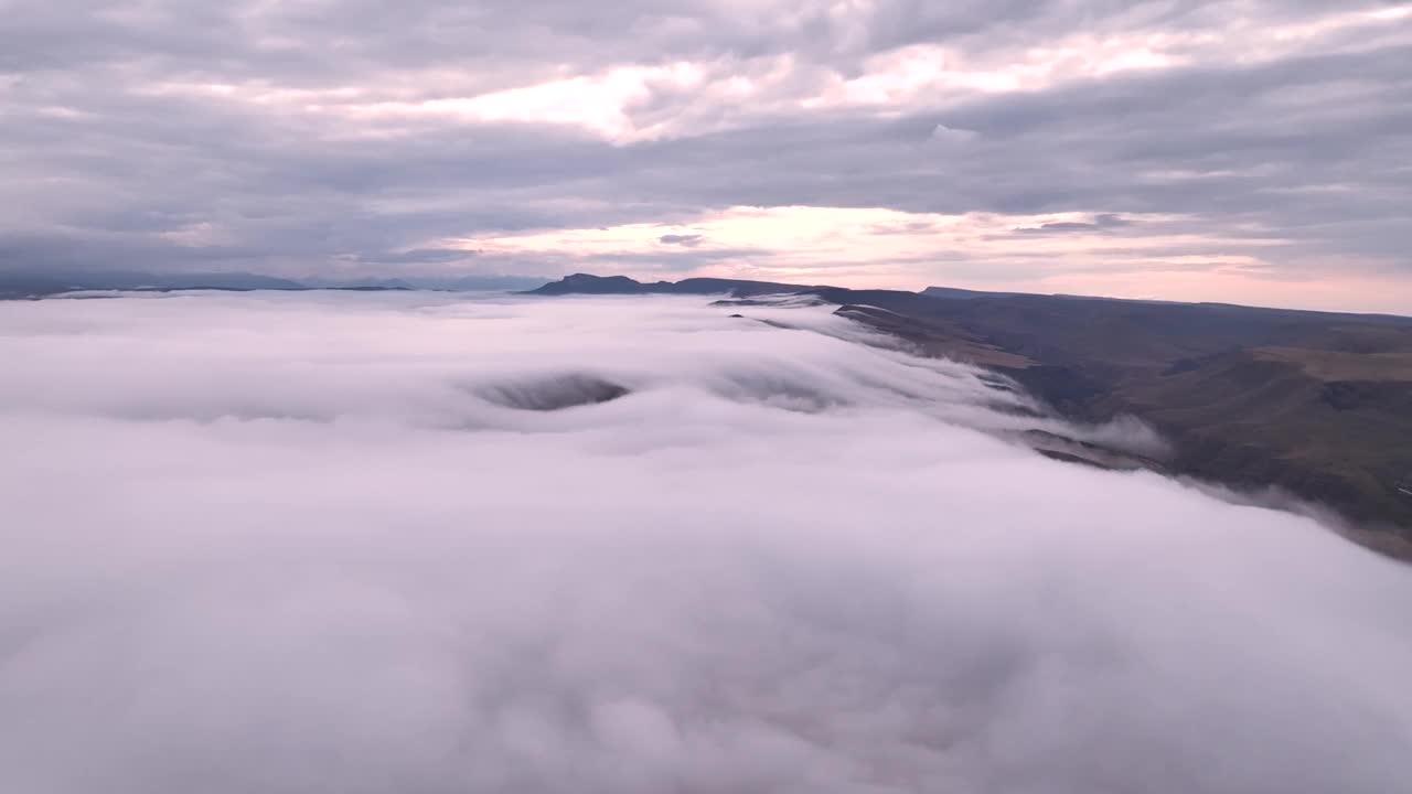 无人机飞越云山的视频。云雾缭绕在山林之上，云彩顺着山谷流下，融入夕阳的余晖视频下载