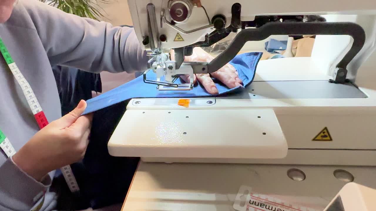纺织工业。圈和纽扣。工业缝纫设备，一种打环的机器。这个女孩在一件蓝色衬衫上打环视频素材
