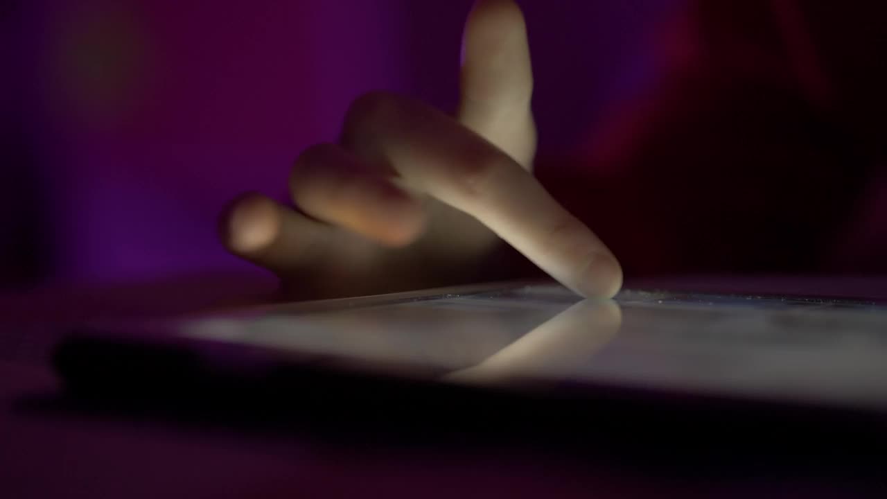 女孩在晚上用手指浏览数码平板电脑。使用智能手机，浏览社交网络的人。近距离手指滚动社交媒体应用程序或阅读新闻动态在线。视频下载