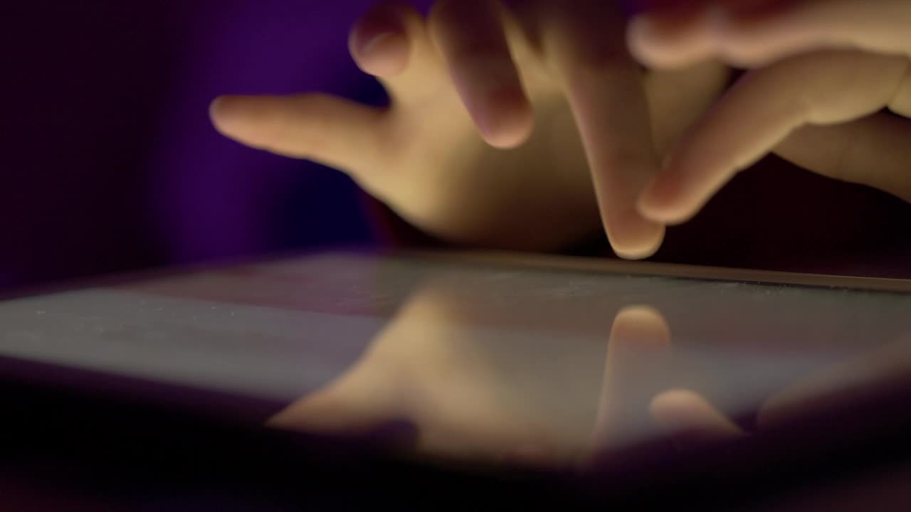 女孩晚上在触摸屏数码平板电脑上打字。在移动电脑上输入文章、文本或文件的人的手近距离。人的手打字文本信息电子邮件在平板电脑触摸屏键盘。视频下载
