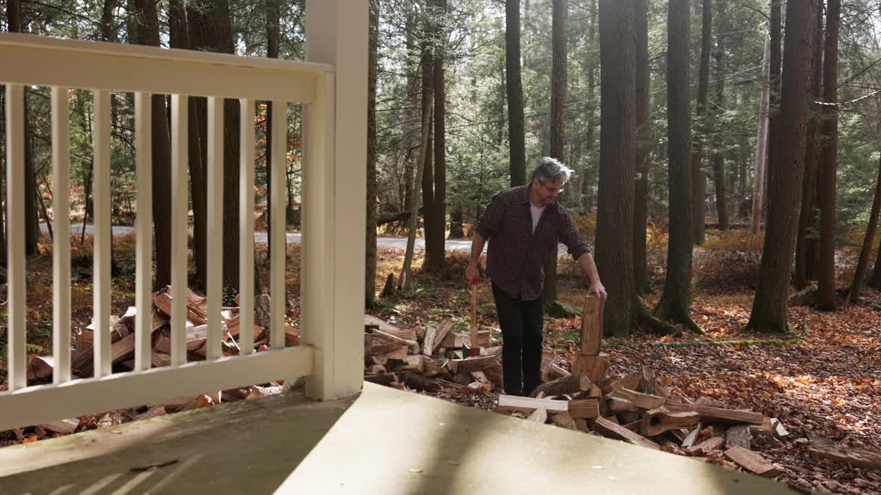 在阳光明媚的树林里，一个银发男子在自家后院用斧头砍柴。慢动作视频下载