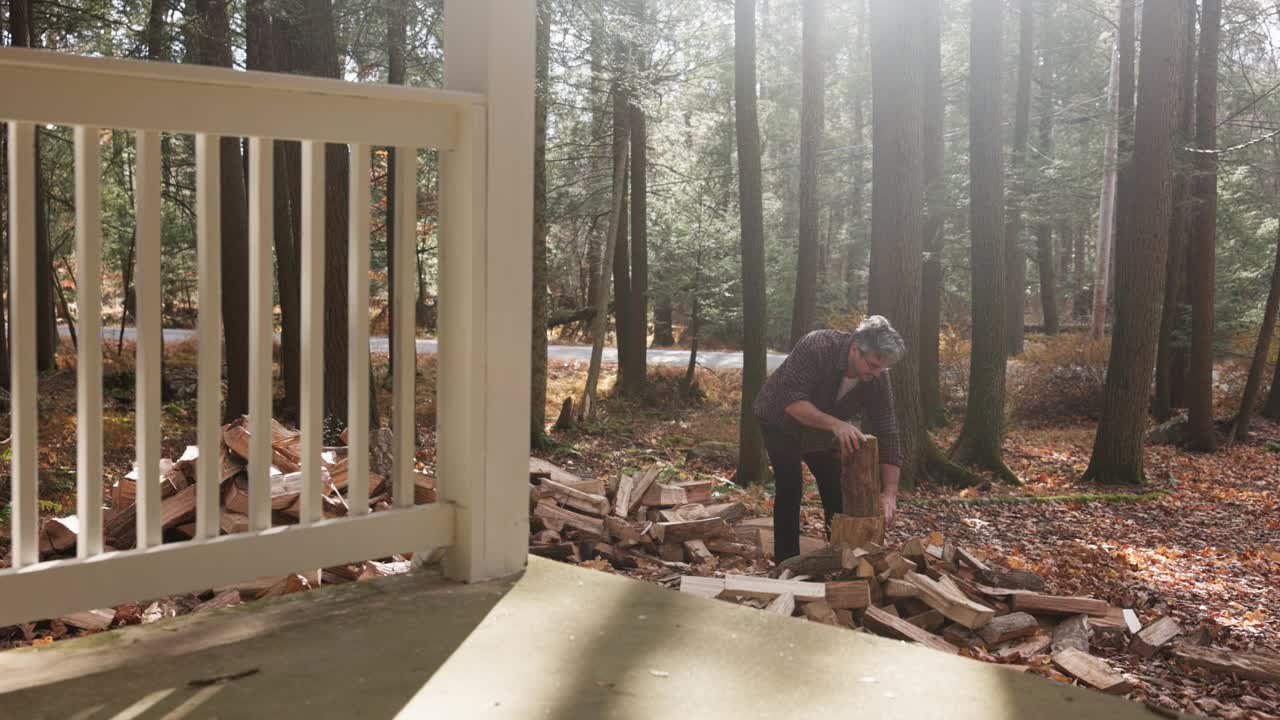 柴火堆垛。一名男子在小屋外砍柴，准备在阳光充足的林地里过冬。慢动作视频下载