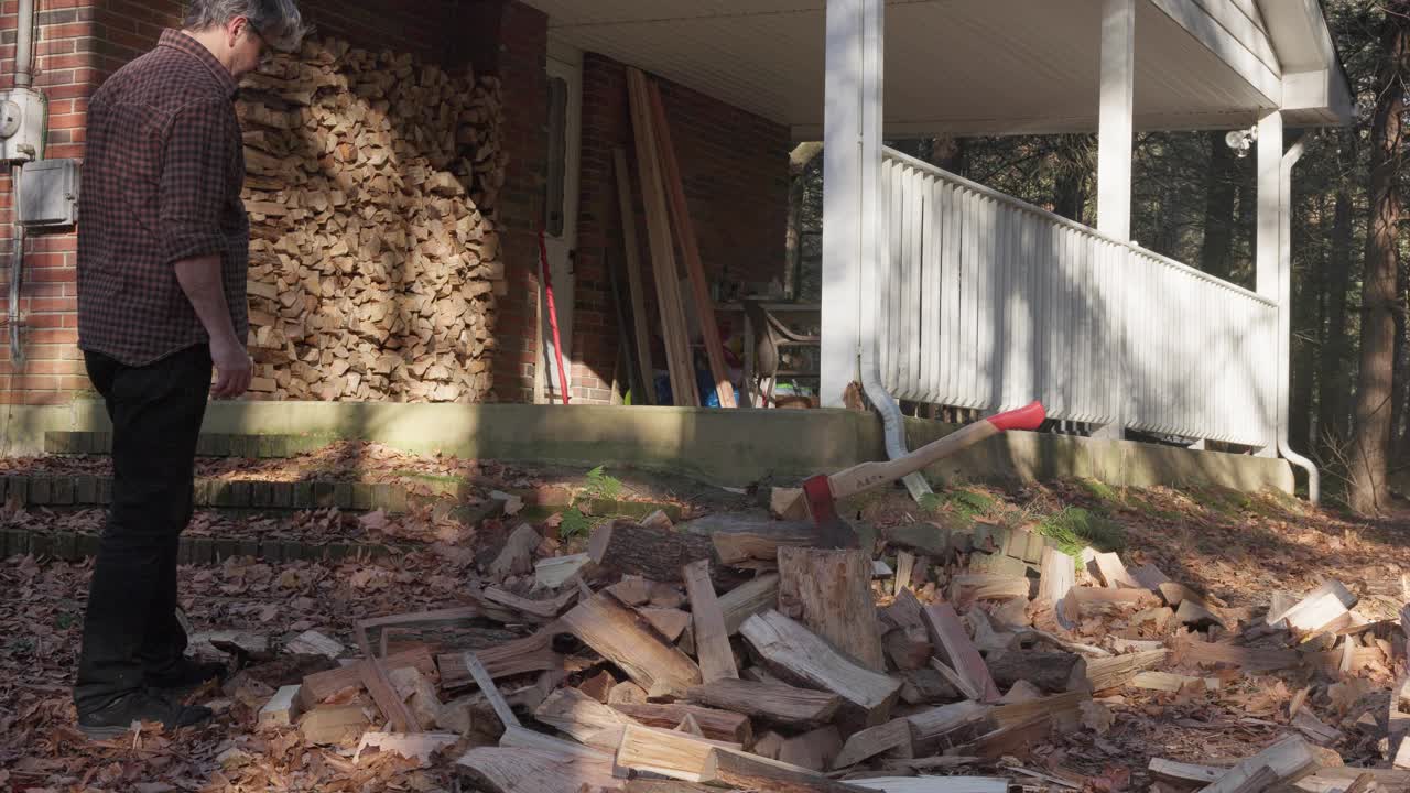 柴火准备。一个成熟的男人在森林里捡拾成堆的柴火，把它们堆在砖房前的柴堆里视频下载