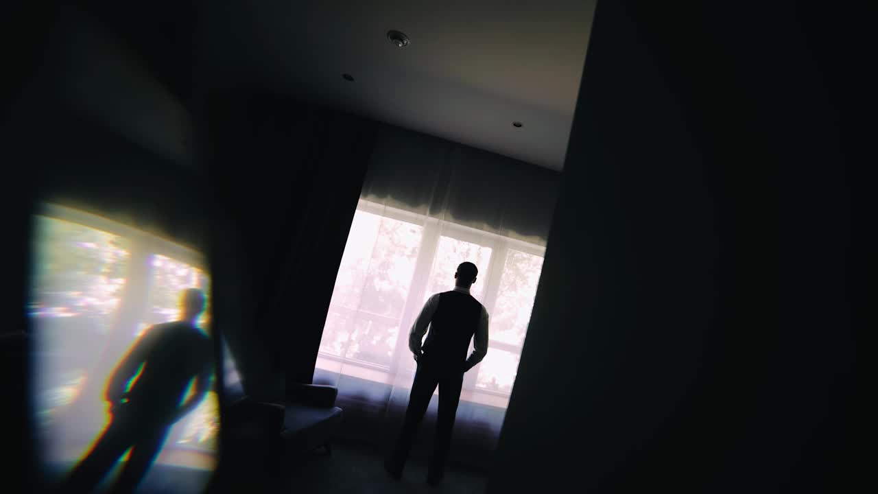 一个男人的剪影，站在房间明亮的窗前，透过窗户望向街道。神秘的轮廓视频下载