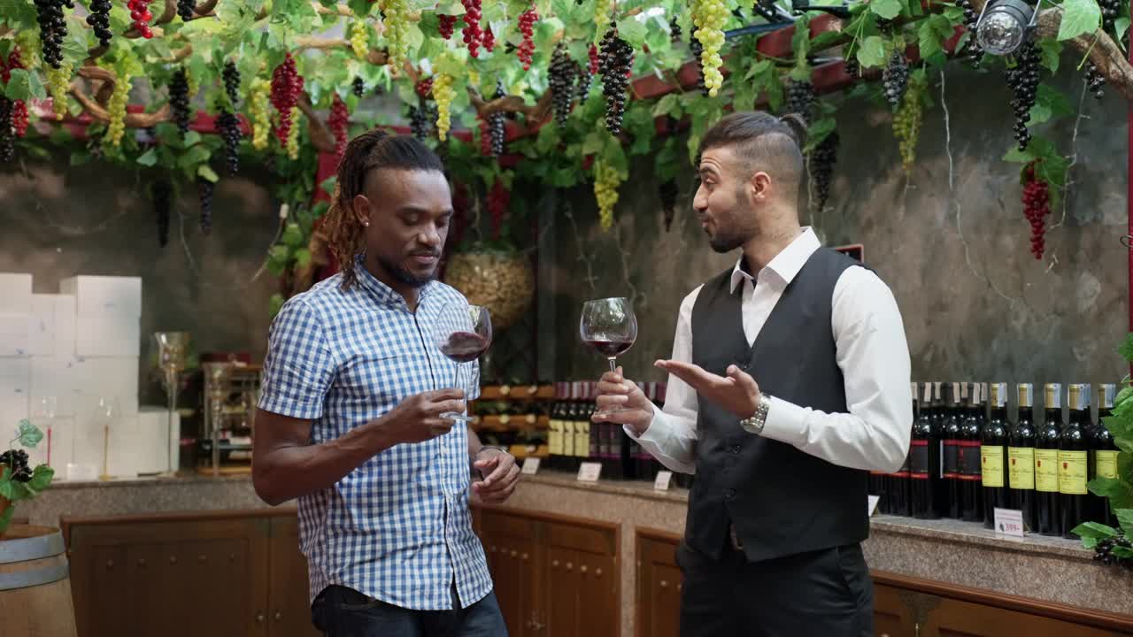 图为，非洲黑人商人和专业的南亚侍酒师在酿酒师工厂的仓库里品尝一杯红酒，以测试红酒的质量。仓库周围是葡萄树上的葡萄，为秋天的收获而成熟。视频下载