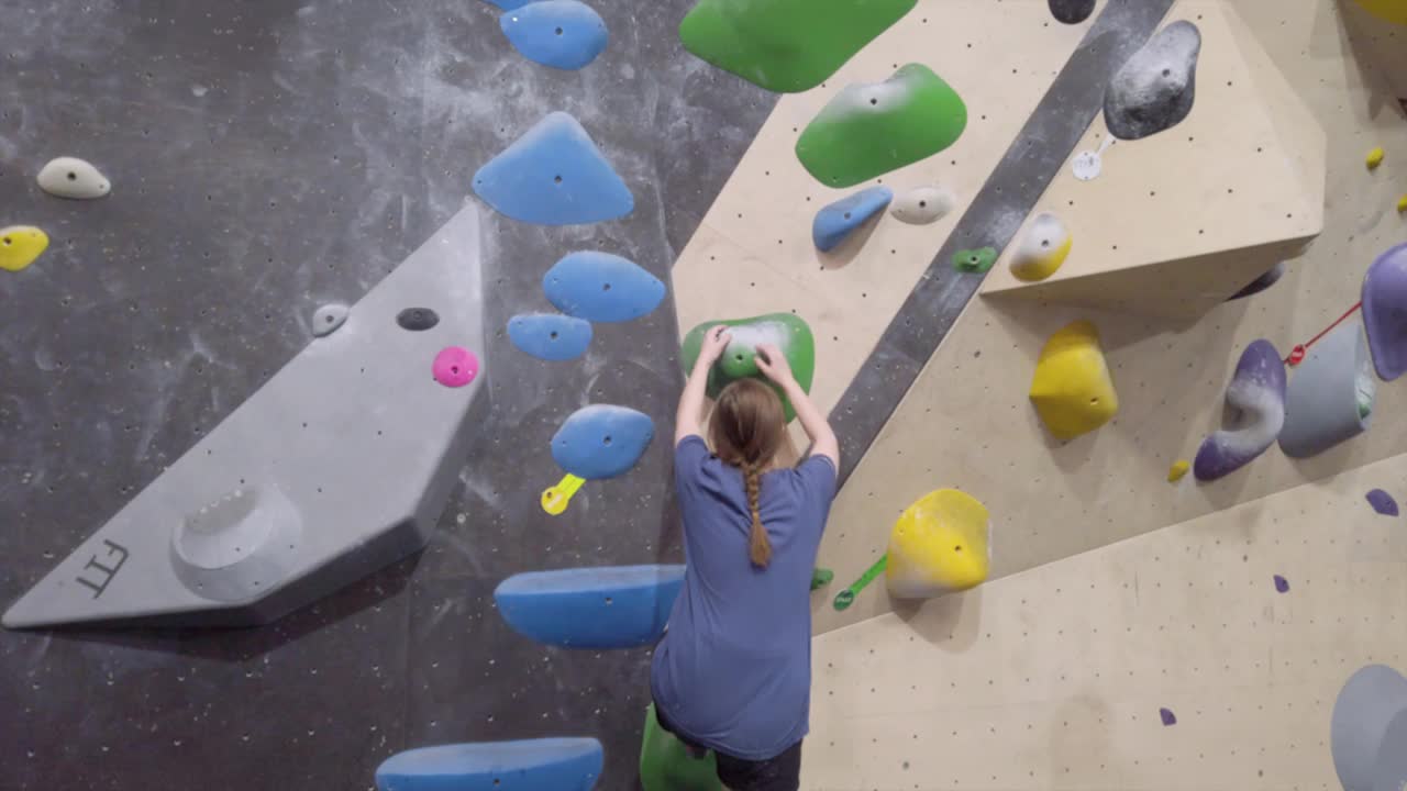 年轻的攀登者女孩在健身房攀爬室外抱石墙。视频下载