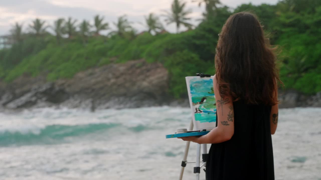 女艺术家在暴风雨的海滩上用帆布画海景。浪撞，风吹，创意的爱好捕获。艺术女人专注，创造海岸艺术，被自然美景包围。缓慢的运动。视频下载