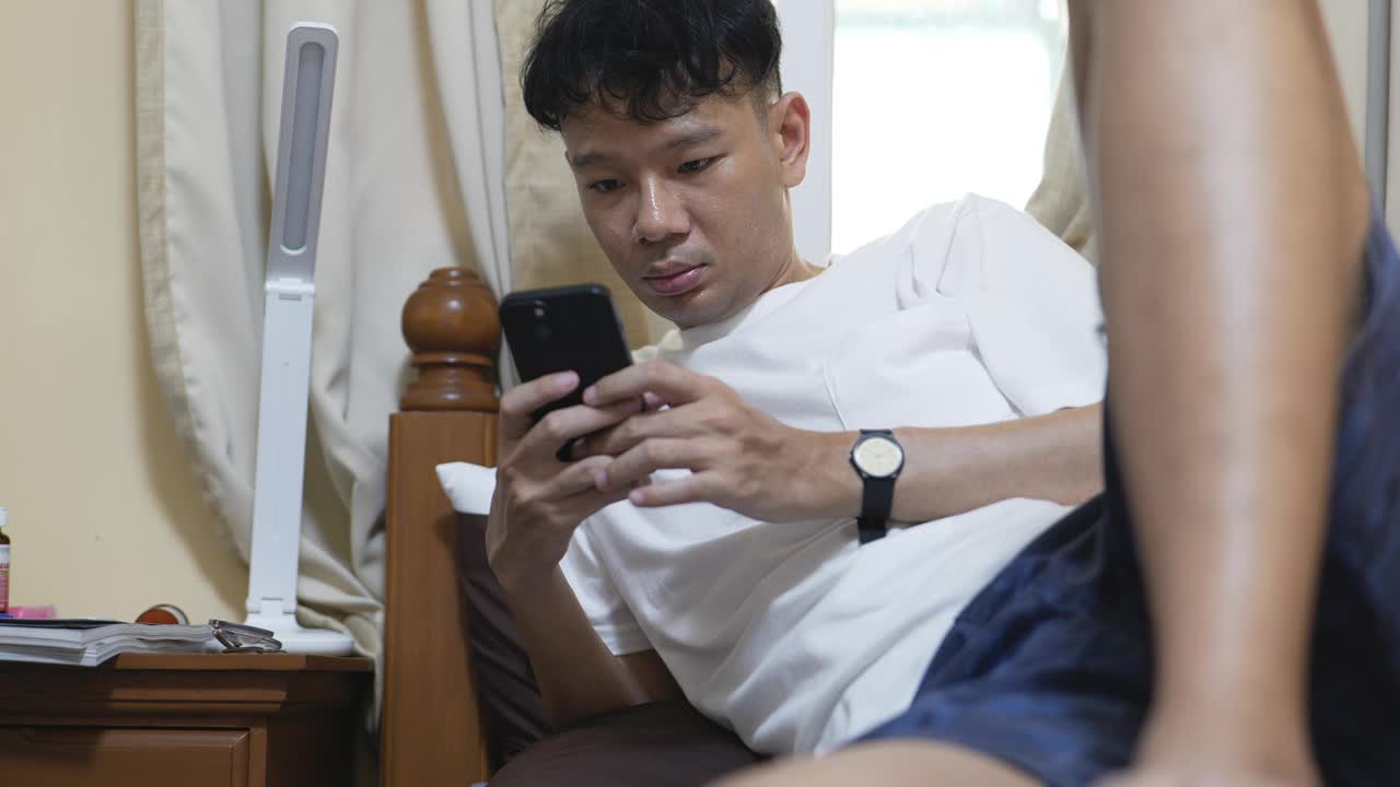 亚洲男子在床上玩智能手机视频下载