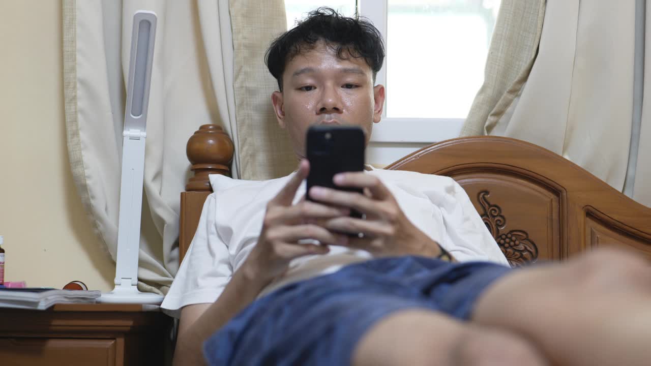 亚洲男子在床上玩智能手机视频下载