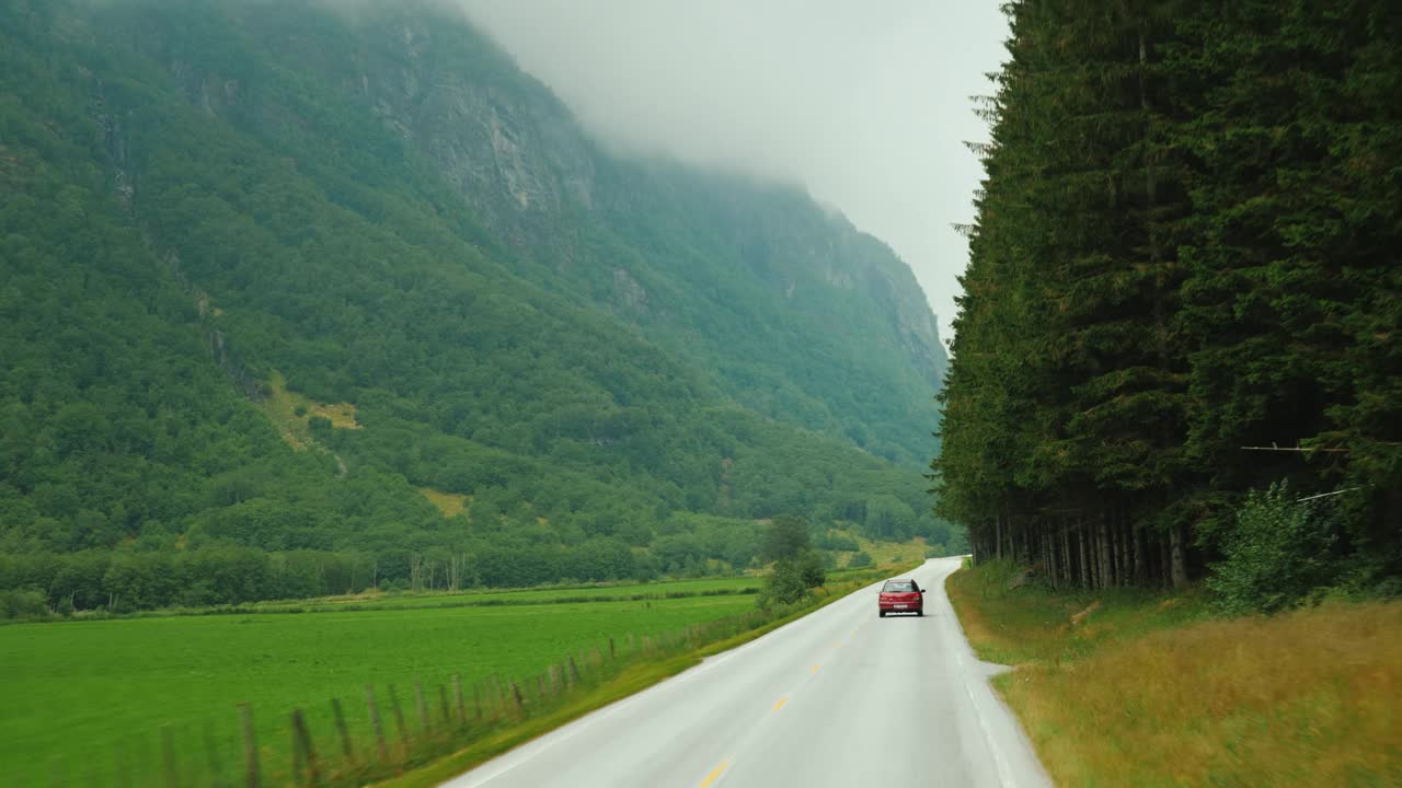 一辆红色的汽车行驶在挪威的一条风景优美的道路上，在绿色的山脉之间视频下载