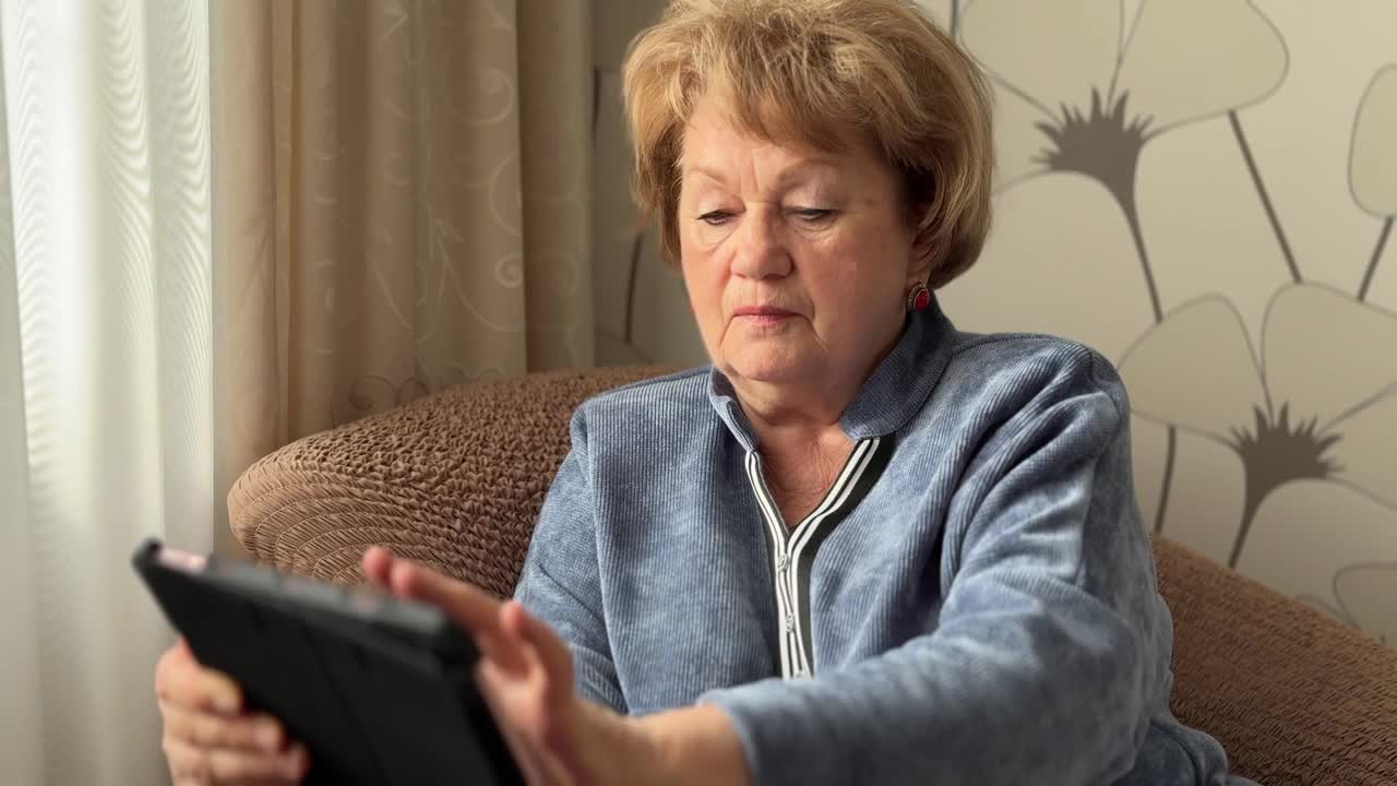 成熟的女人坐在扶手椅上，用电子平板电脑浏览重要信息视频下载