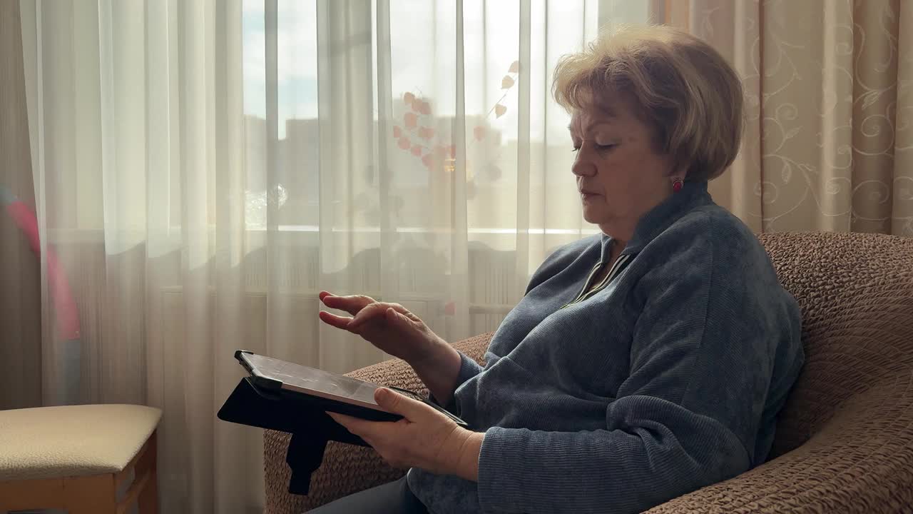 成熟的女人坐在扶手椅上，用电子平板电脑浏览重要信息视频下载
