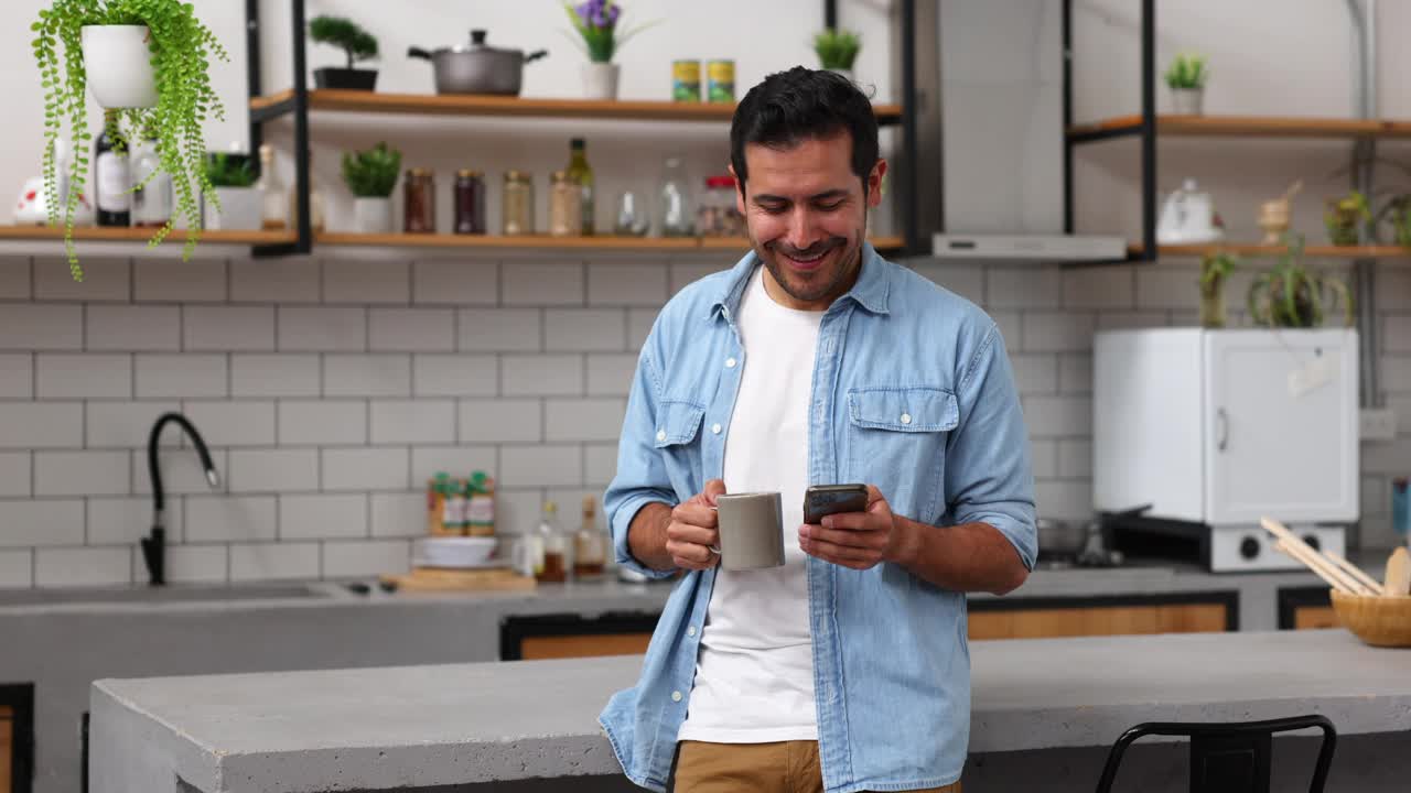 快乐的男人在家里一边喝咖啡一边看手机上的社交媒体视频下载