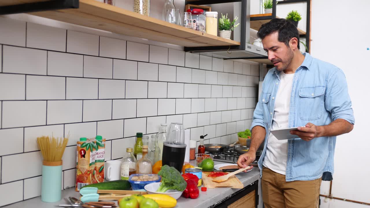 一名拉丁美洲男子在家里用电子平板电脑按照食谱做饭视频下载