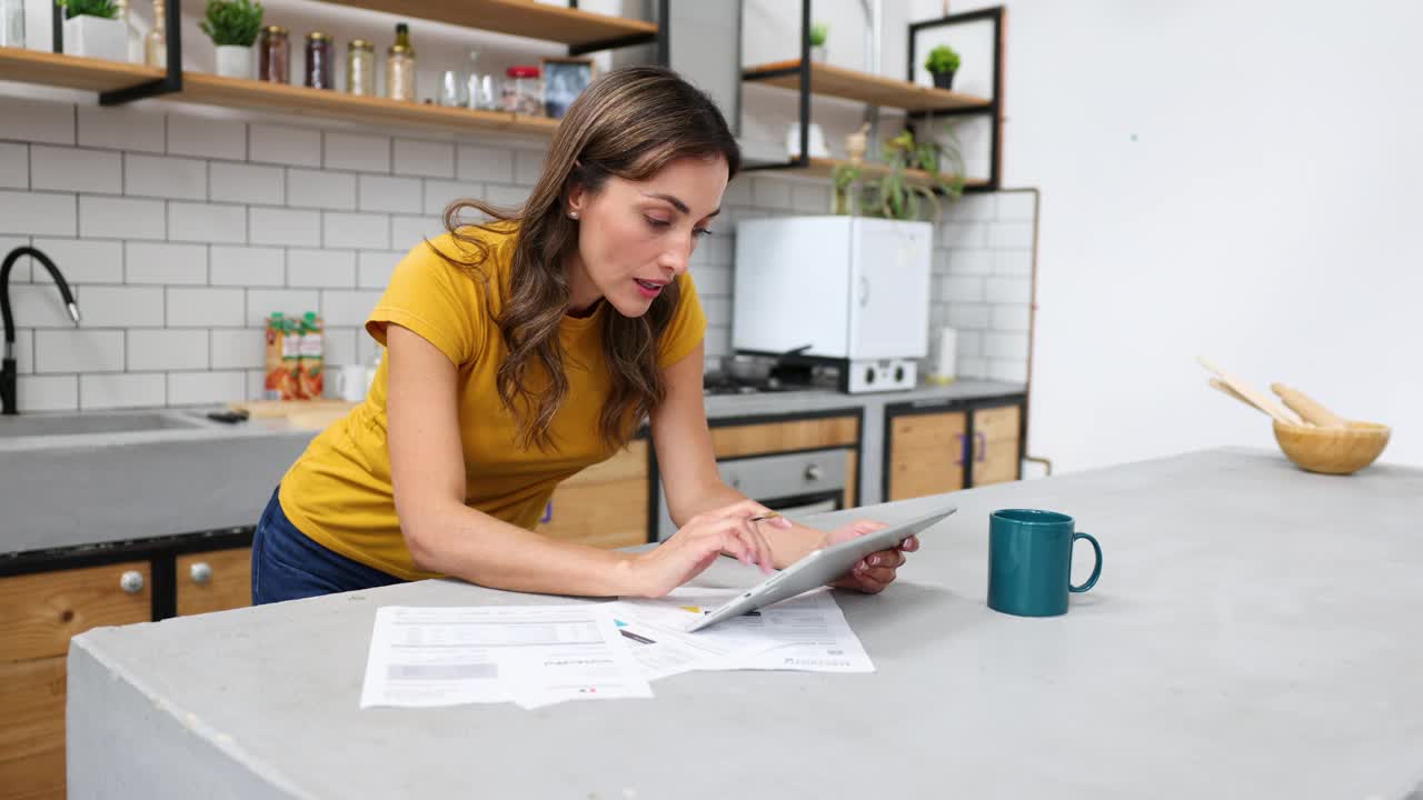 一个漂亮的女人在家工作，看起来非常专注地使用一些文件和数字平板电脑视频下载