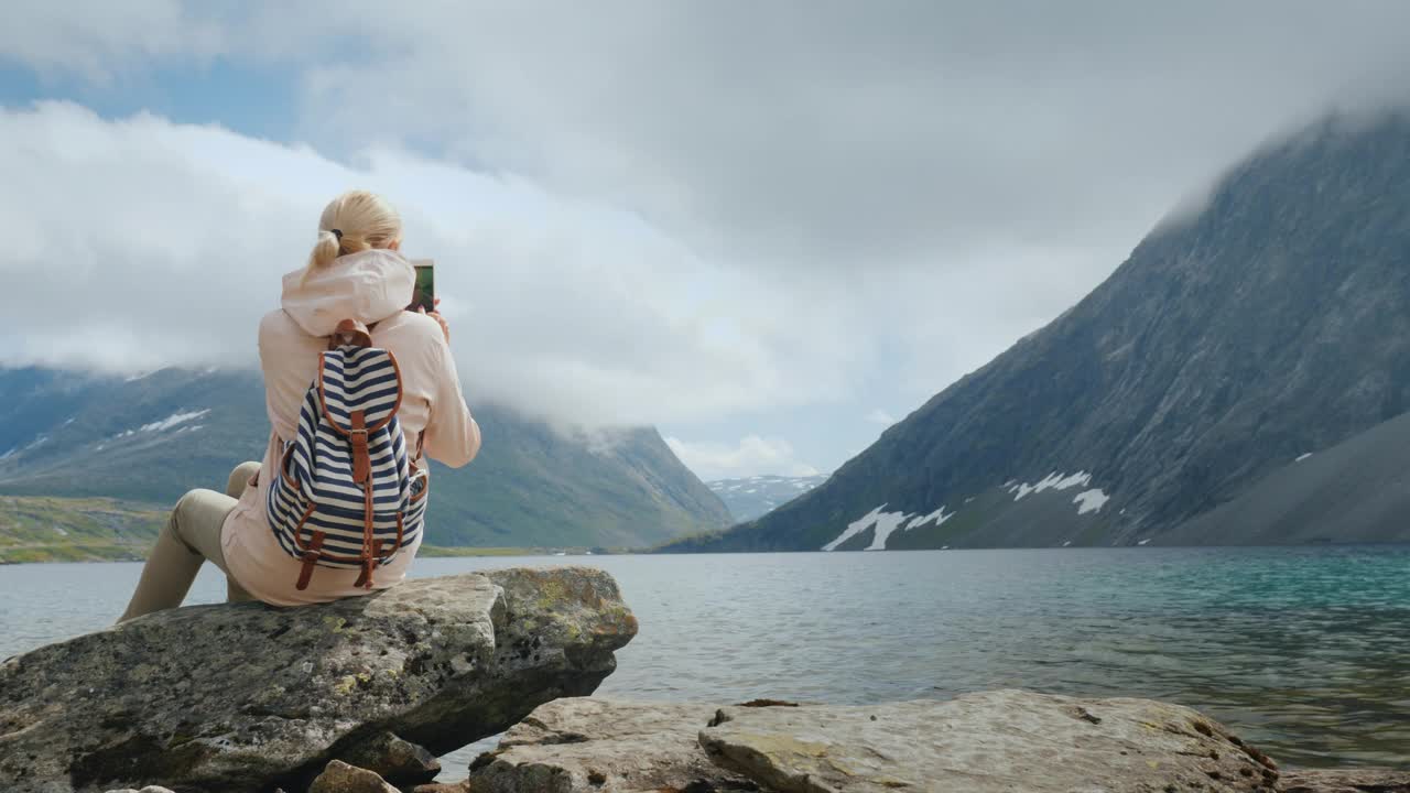 一位妇女正在拍摄挪威高山湖泊的美景。在世界的边缘度假视频下载