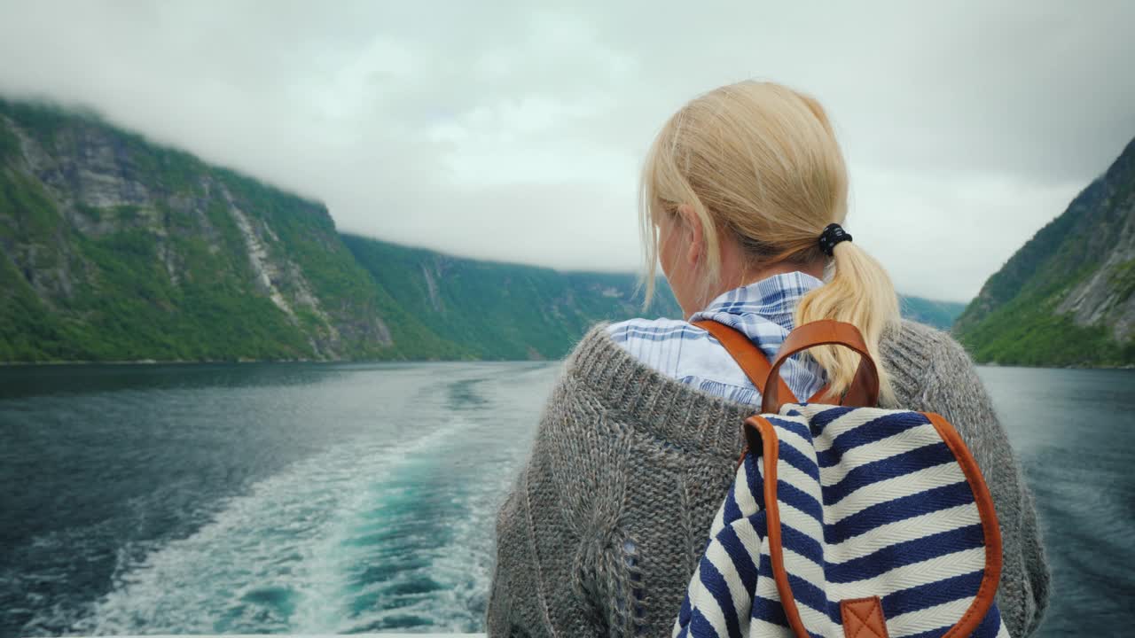 一个女人站在一艘游轮的船尾，看着退去的岩石和峡湾的海浪视频下载