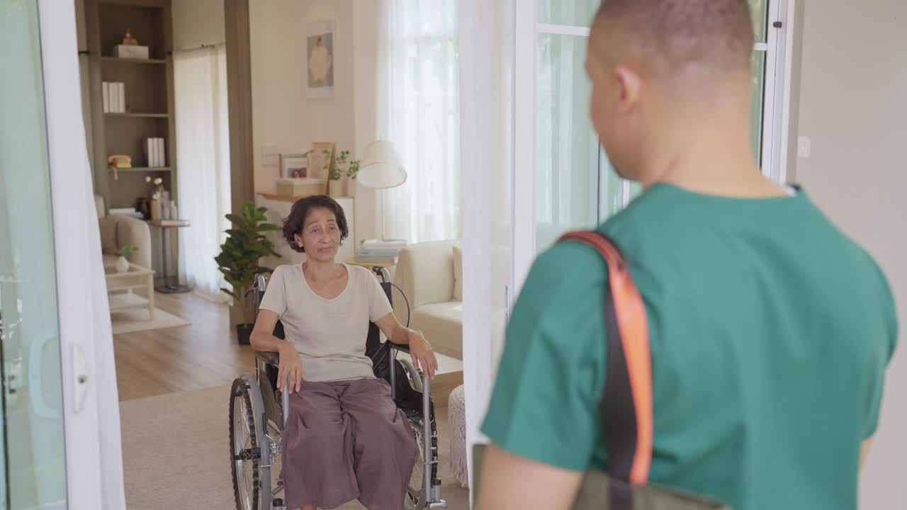 一个泰国老年女病人的特写镜头，穿着便服，笑容灿烂地迎接一个家庭保健医生进入病人舒适的客厅。视频下载