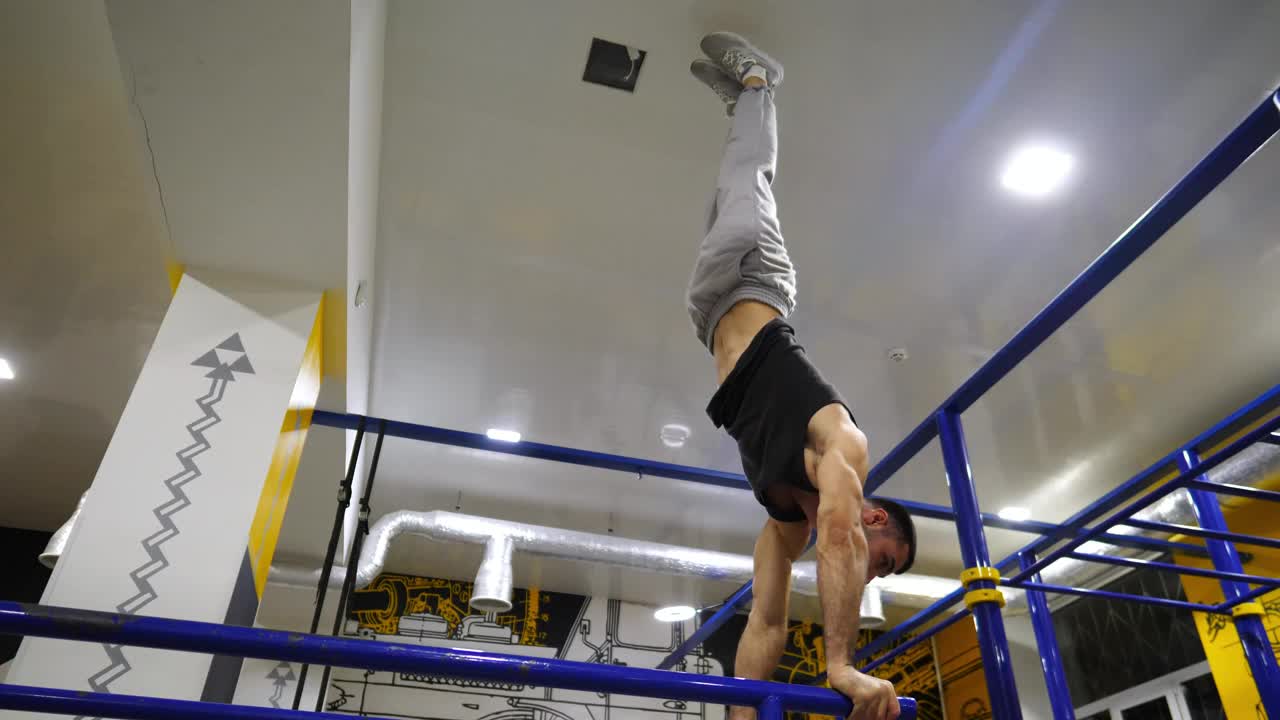 强壮的肌肉男在现代健身房的双杠上倒立。男体操运动员在健身中心的高低杠上做高难度动作。年轻运动员正在表演。运动生活方式的概念视频下载