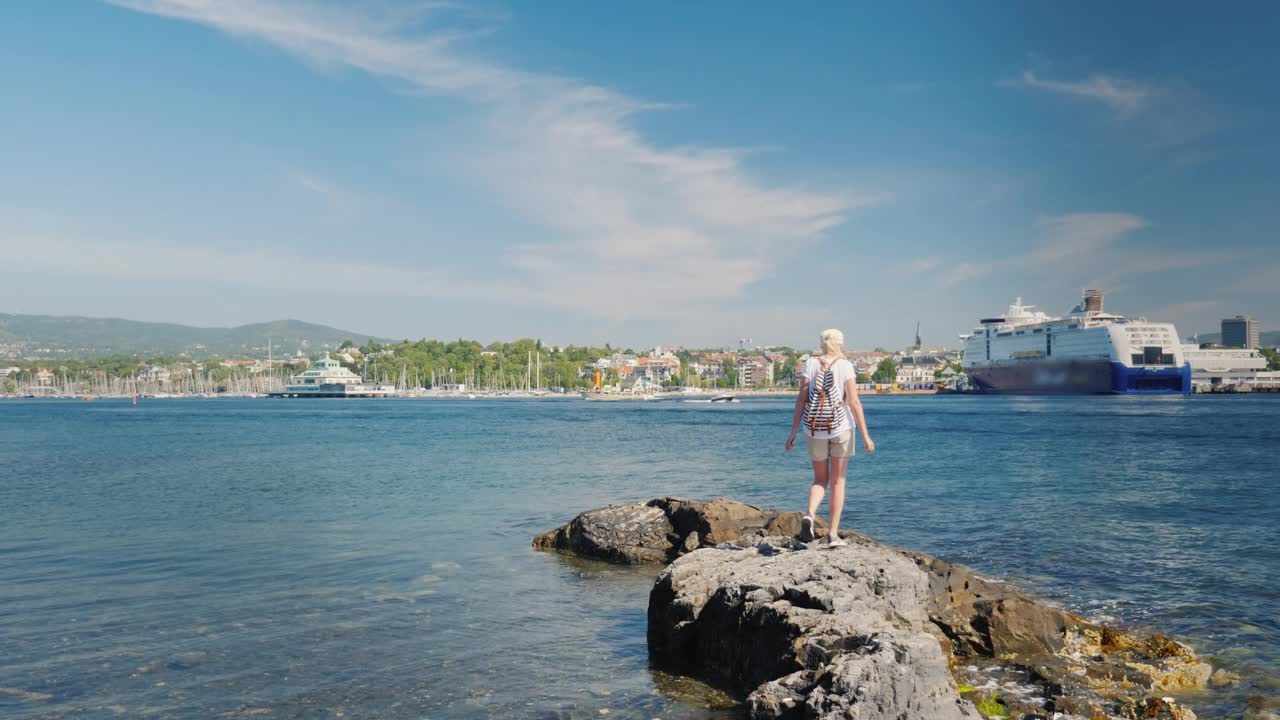 一名女子在水中的岩石上行走，背景是挪威的奥斯陆市视频下载