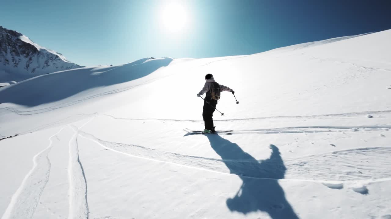 运动FPV无人机跟随一名穿着白色夹克的男性滑雪者，在一个极端的山上自由骑行，从冬季山上的冰川移动视频下载