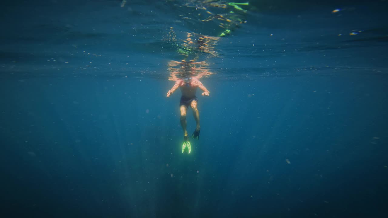 蓝色背景下的水下潜水员。穿着短裤和脚蹼的年轻人在阳光下潜到海底，慢动作视频下载