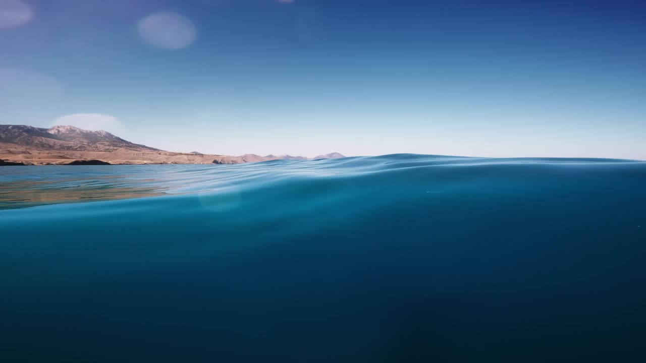 海洋的抽象视频背景，水下部分和太阳照在上面，由水线划分。美丽晴朗的天空，山脉和明亮的阳光照耀在海水上视频下载