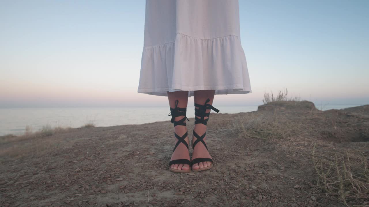 年轻性感苗条的女人在海边的一个岛上摆姿势，穿着白色连衣裙和黑色凉鞋，打着领带。海滩度假时的希腊风格服装视频下载
