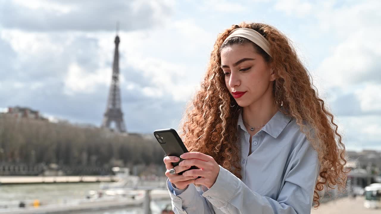 巴黎的年轻卷发女人在用智能手机视频下载
