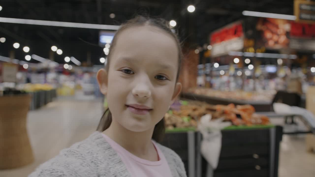 可爱的孩子在超市打在线视频电话，一边说话一边挥手，看着镜头里的食物视频下载