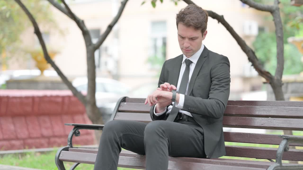 商人坐在长凳上使用智能手表视频下载